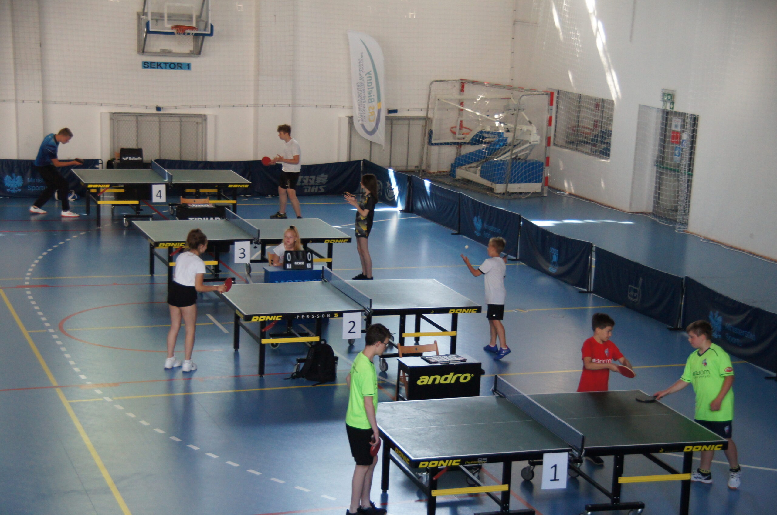 Zawodnicy grający w tenisa stołowego w hali sportowej.